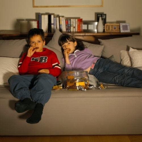 Kids on a couch eating snacks and watching a screen