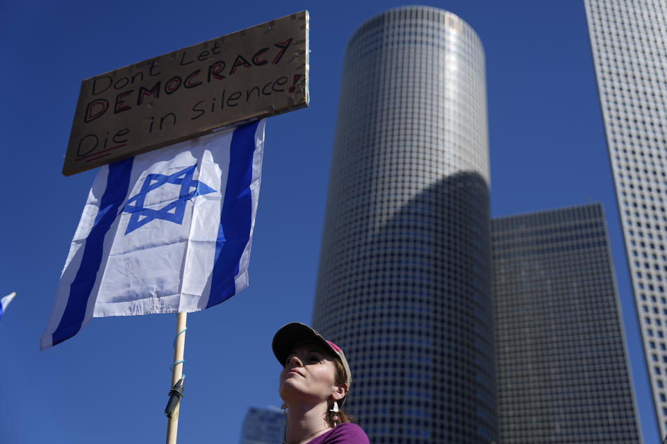 A demonstrator waves a banner and the Israeli flag during a protest against plans by Prime Minister Benjamin Netanyahu's new government to overhaul the judicial system, in Tel Aviv, Israel, Thursday, March 9, 2023. (AP Photo/Ariel Schalit)
