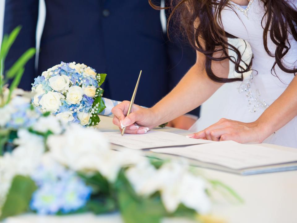 Bride signs marriage license with white and blue bouquets in foreground