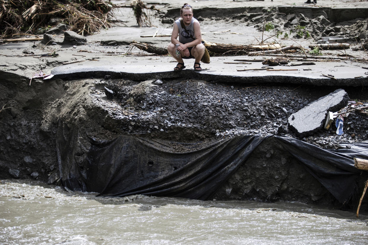 A woman looks at the remains of a road that was washed away by floodwaters.