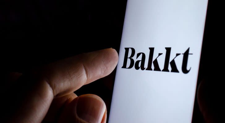 A finger touching a phone screen with the Bakkt logo on it.