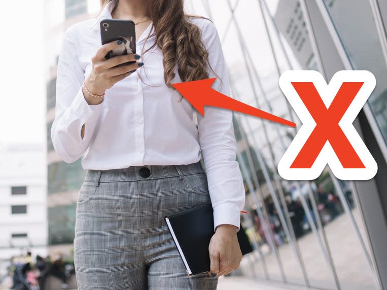 x over woman wearing a white button down and trousers while texting and walking