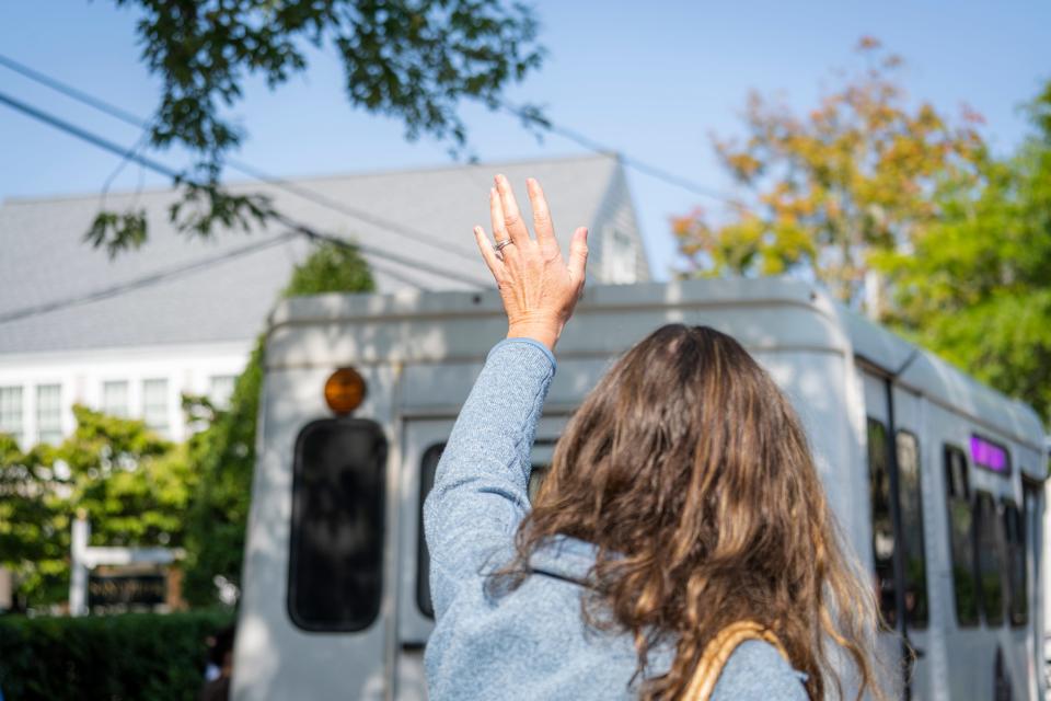 A person is seen, from behind, waving at a bus.