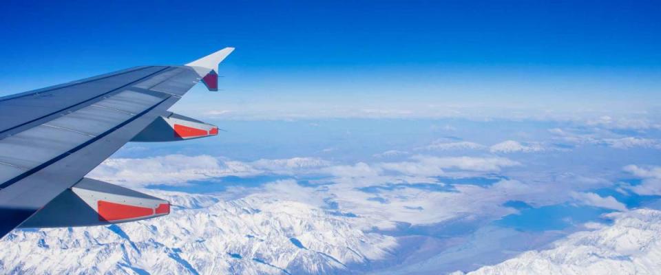 Flying over snow capped mountains, view of airplane wing