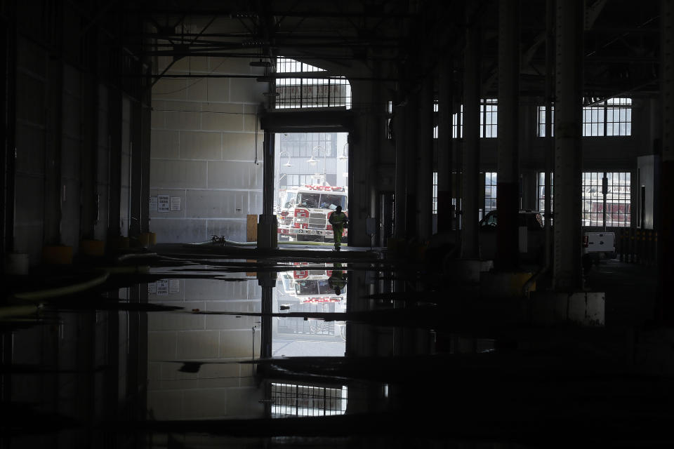 A fire official is shown reflected in a puddle in a warehouse after a fire broke out before dawn at Fisherman's Wharf in San Francisco, Saturday, May 23, 2020. Fire officials said no injuries have been reported Saturday morning and firefighters are making multiple searches to ensure no one was inside the building on Pier 45. (AP Photo/Jeff Chiu)