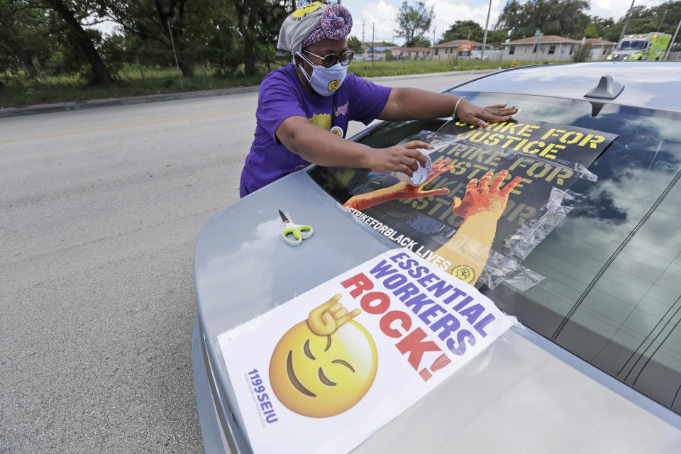 Union member Margalie Williams tapes a sign on her car as she participates in a caravan to hand out masks to prevent the spread of the new coronavirus and lunches to workers at the Franco Nursing & Rehabilitation Center, Monday, July 20, 2020, in Miami. Most facilities, experts and industry leaders told The Associated Press that a statewide mask mandate would help protect staff members, and consequently residents, from the virus. (AP Photo/Wilfredo Lee)