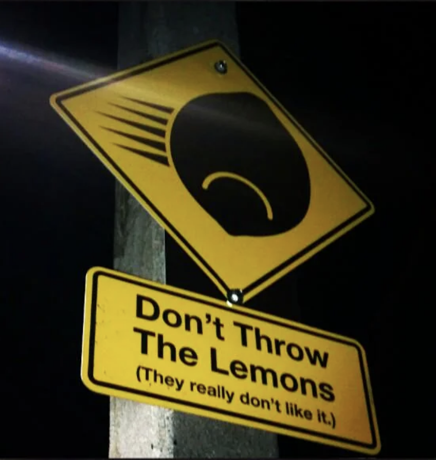 A street sign with a speeding lemon illustration and a cautioning face. The text reads, 
