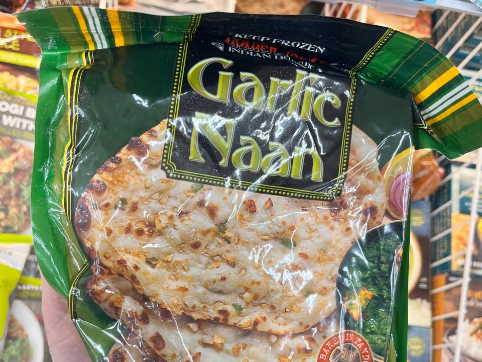 A hand holding a bag of Trader Joe's garlic naan in the freezer section.