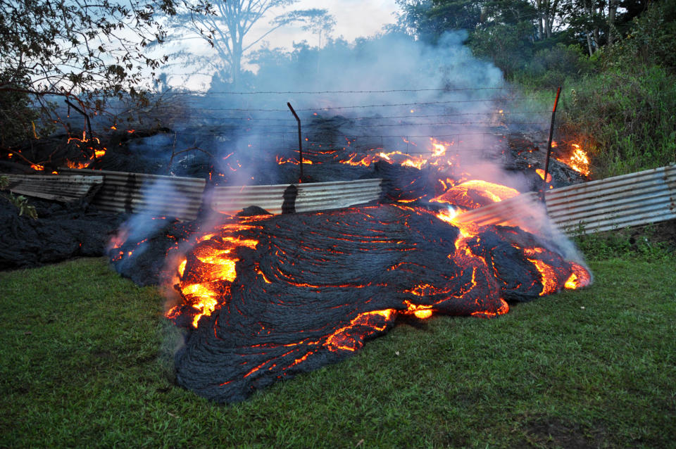 This Tuesday, Oct. 28, 2014 photo provided by the U.S. Geological Survey shows lava that has pushed through a fence marking a property boundary above the town of Pahoa on the Big Island of Hawaii. After weeks of slow, stop-and-go movement, a river of asphalt-black lava was less than the length of a football field from homes in the Big Island community Tuesday. The lava flow easily burned down an empty shed at about 7:30 a.m., several hours after entering a residential property in Pahoa Village, said Hawaii County Civil Defense Director Darryl Oliveira. A branch of the molten stream was less than 100 yards (90 meters) from a two-story house. It could hit the home later Tuesday if it continues on its current path, Oliveira estimated. Residents of Pahoa Village, the commercial center of the island's rural Puna district south of Hilo, have had weeks to prepare for what's been described as a slow-motion disaster. Most have either already left or are prepared to go. (AP Photo/U.S. Geological Survey)