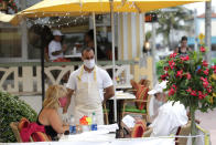 Jeffrey Holinka wears a protective face mask as he waits to receive an order at the On Ocean 7 Cafe along Ocean Drive in Miami Beach, Fla. during the new coronavirus pandemic, Wednesday, May 27, 2020. Ocean Drive was closed to traffic as restaurants in Miami Beach reopened Wednesday after being closed to mitigate the spread of the coronavirus. (AP Photo/Lynne Sladky)