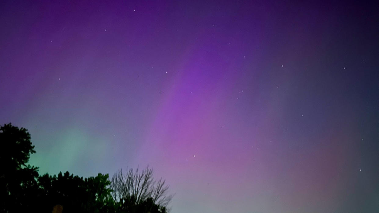  Photo of the northern lights, showing light green and purple lights in a dark night sky. 