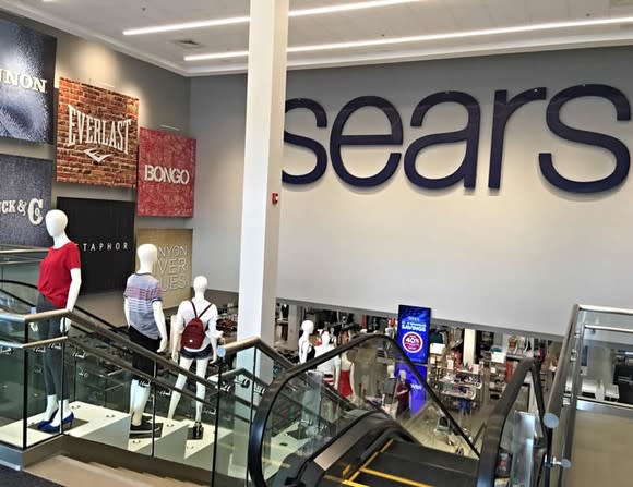 An entrance to a Sears store, as seen from an escalator landing one floor up.