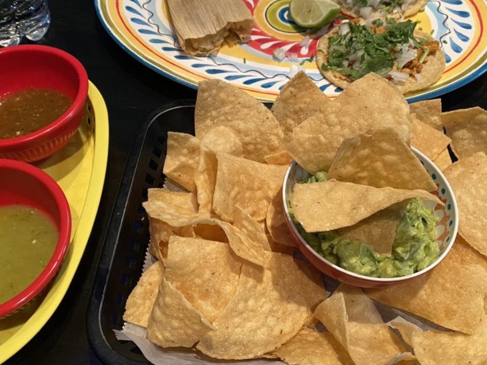 A tray of chips with guacamole in the centre, on a table with other dishes.
