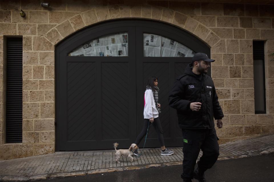 A private security guard stands nearby as a woman walks her dog past the house of ex-Nissan chief Carlos Ghosn in Beirut, Lebanon, Friday, Jan. 3, 2020. The former Nissan Motor Co. Chairman fled Japan this week while awaiting trial on financial misconduct charges and appeared in Lebanon. (AP Photo/Maya Alleruzzo)