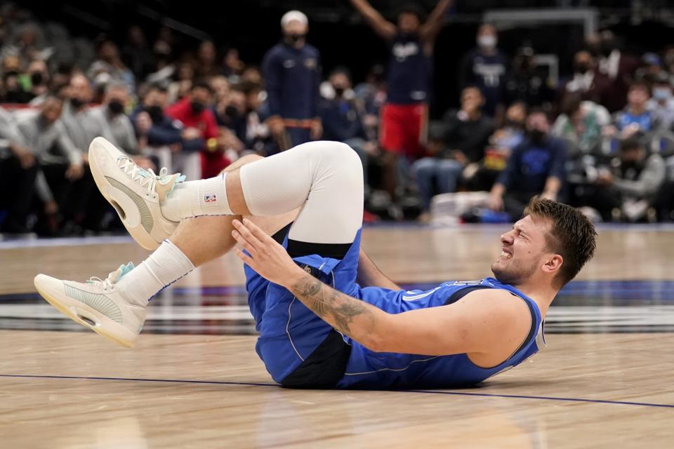 Dallas Mavericks guard Luka Doncic reaches for his left leg after taking a spill in the second half of an NBA basketball game against the New Orleans Pelicans in Dallas, Friday, Dec. 3, 2021. (AP Photo/Tony Gutierrez)