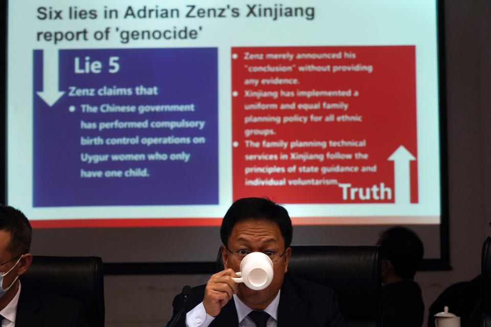 Xu Guixiang, a deputy spokesperson for the Xinjiang regional government, drinks from a cup near a slide refuting claims of genocide during a press conference in Beijing, China. The Chinese official on Monday denied Beijing has imposed coercive birth control measures among Muslim minority women, following an outcry over a tweet by the Chinese Embassy in Washington claiming that government polices had freed women of the Uighur ethnic group from being "baby-making machines." (AP Photo/Ng Han Guan)