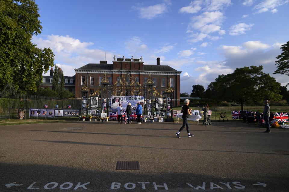 A woman runs by portraits and messages of remembrance for Princess Diana displayed on the gates of Kensington Palace, in London, Wednesday, Aug. 31, 2022. Wednesday marks the 25th anniversary of Princess Diana's death in a Paris car crash. (AP Photo/Alastair Grant)