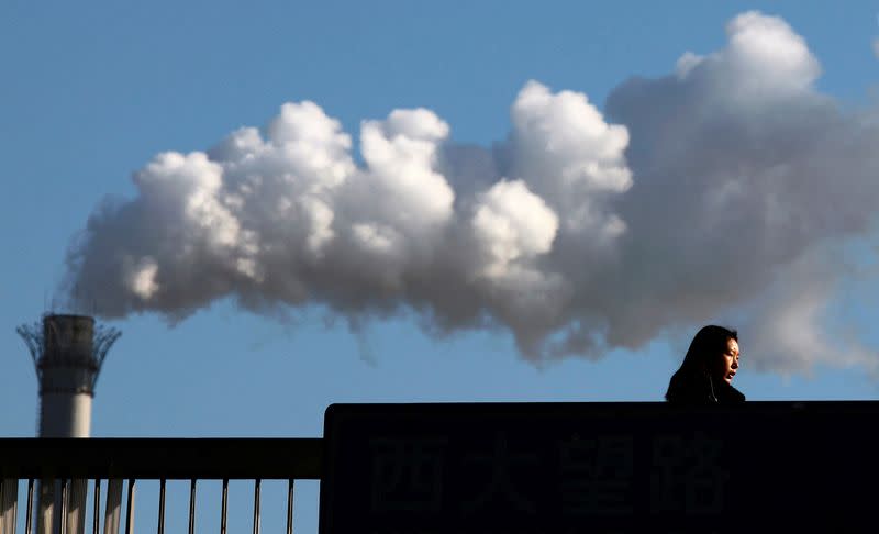 FILE PHOTO: A woman walks across a bridge in front of a chimney billowing smoke from a coal-burning power station in central Beijing.