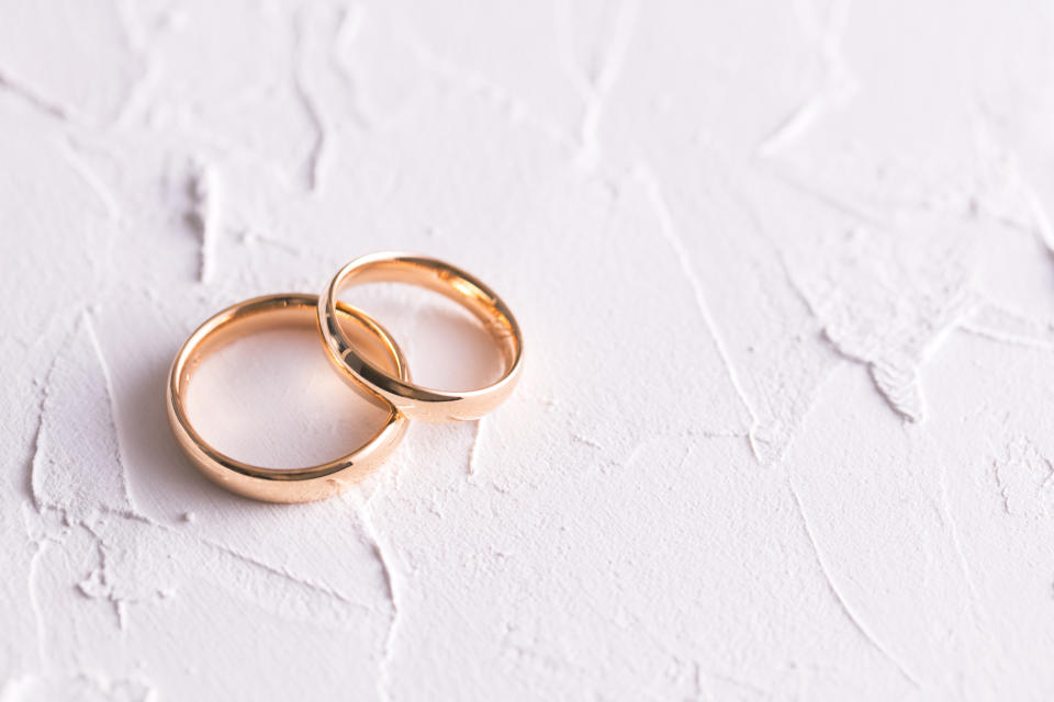 Two gold wedding bands on a textured white surface, symbolizing marriage and commitment