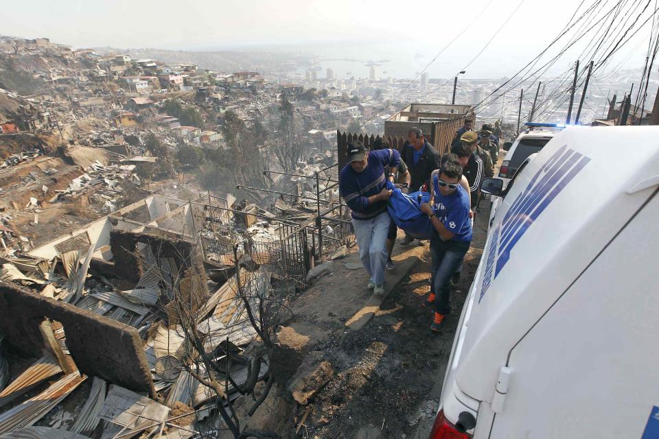 Residents and rescue workers carry a body from the place where a forest fire burned several neighbourhoods in the hills in Valparaiso city, northwest of Santiago, April 13, 2014. At least 11 people were killed and 500 houses destroyed over the weekend by a fire that ripped through parts of Chilean port city Valparaiso, as authorities evacuated thousands and used aircraft to battle the blaze. REUTERS/Eliseo Fernandez (CHILE - Tags: SOCIETY ENVIRONMENT DISASTER TPX IMAGES OF THE DAY)