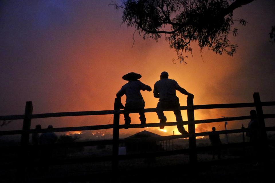 In this Sunday, Jan. 29, 2017 photo, residents watch nearby wildfires in Portezuelo, Chile. Strong winds have continued to stoke the flames of the raging wildfires in Chile. Firefighters and residents fought the fast-spreading blazes on the ground on Tuesday, while a Russian supertanker plane and a Brazilian Hercules dumped thousands of gallons of water on the area. (AP Photo/Esteban Felix)