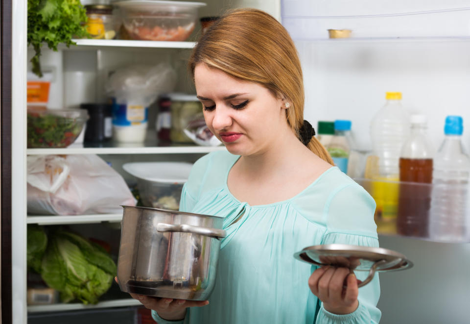 A woman looks on at a foul-smelling pot of food pulled out of the fridge.