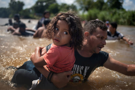 Luis Acosta holds 5-year-old Angel Jesus, both from Honduras, as a caravan of migrants from Central America en route to the United States crossed through the Suchiate River into Mexico from Guatemala in Ciudad Hidalgo, Mexico, October 29, 2018. REUTERS/Adrees Latif/File photo
