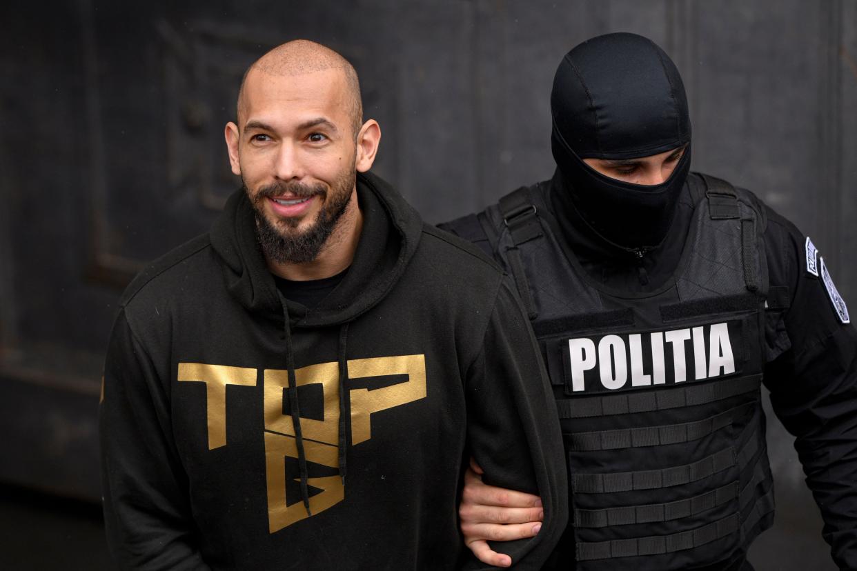 A police officer escorts Andrew Tate, center, handcuffed, from the Court of Appeal in Bucharest, Romania, Tuesday, March 12, 2024. Online influencer Andrew Tate was detained in Romania and handed an arrest warrant issued by British authorities, his spokesperson said Tuesday. (AP Photo/ Alexandru Dobre)