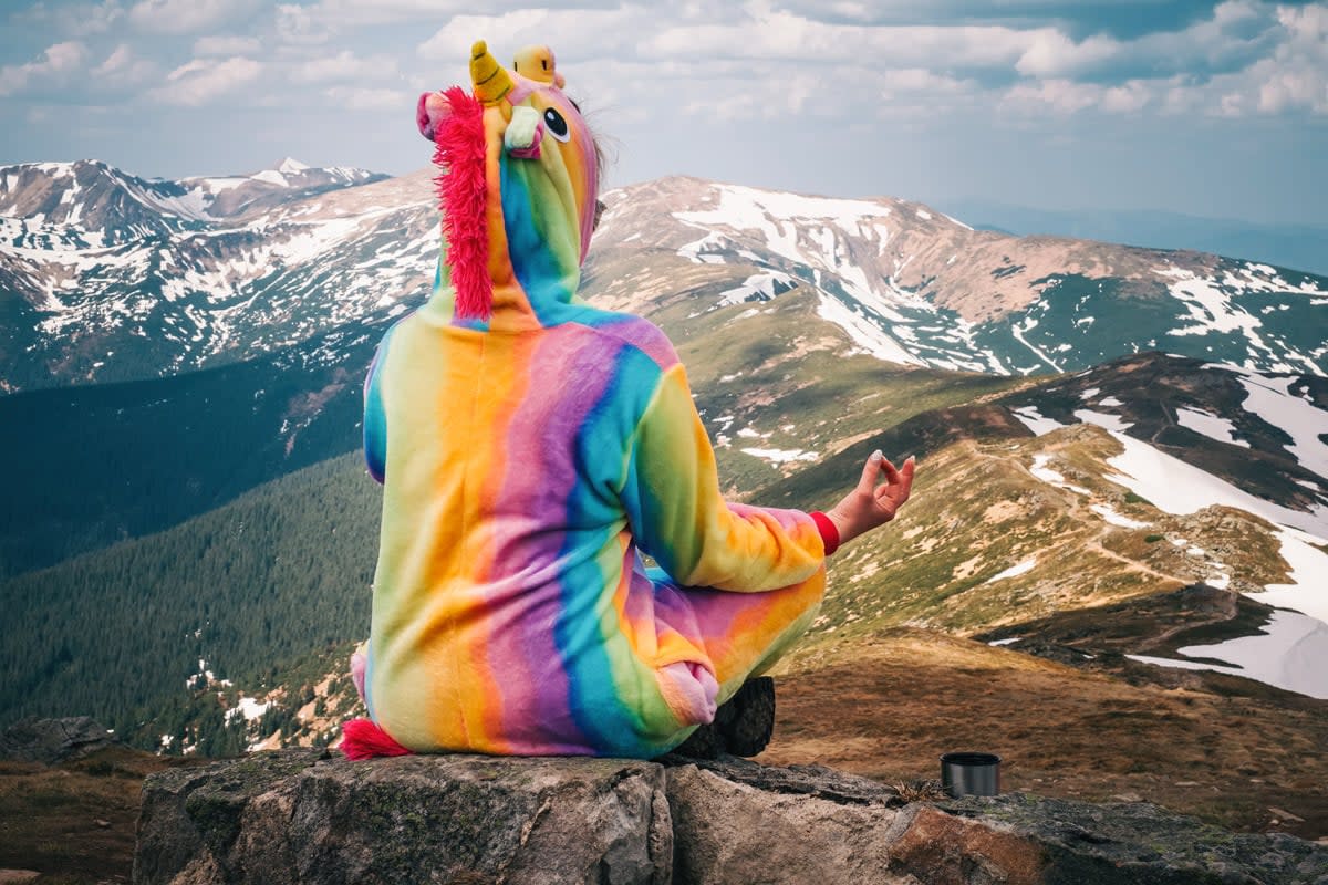 A woman meditates on a mountain top wearing a unicorn outfit. 