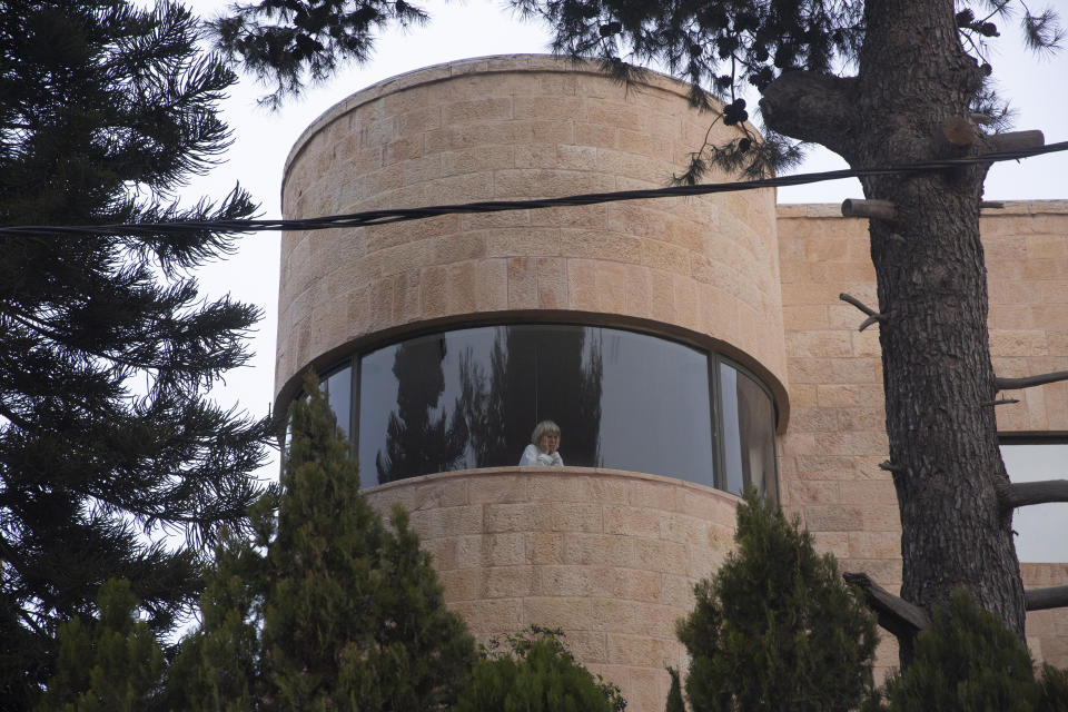 A woman watches Israeli anti-government protesters chant slogans outside of the official residence of Prime Minister Benjamin Netanyahu on the day his corruption trial was originally scheduled before it was postponed, in Jerusalem, Wednesday, Jan. 13, 2021. (AP Photo/Maya Alleruzzo)