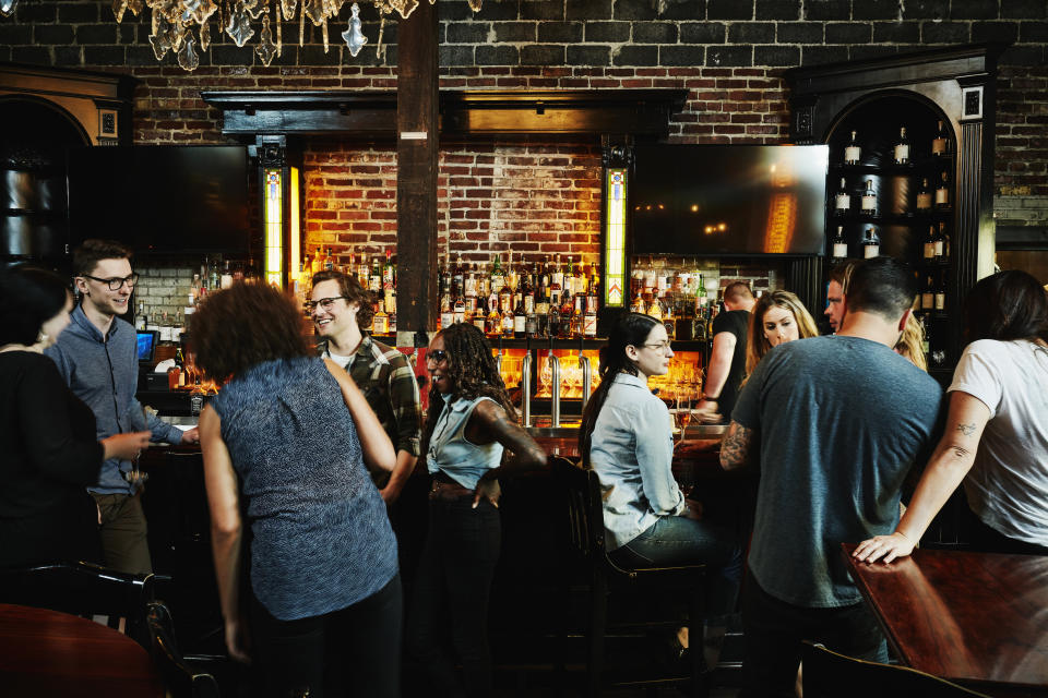 People socializing in a bar with a brick wall and neon signs in the background