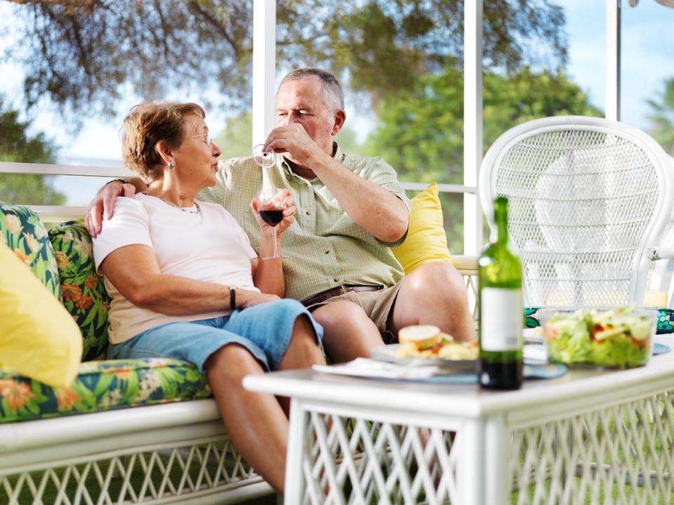 Senior couple sitting on patio furniture with green cushions drinking wine together