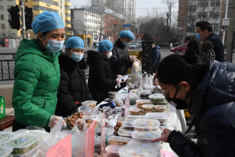 Restaurant workers wear face masks as a preventive measure against the COVID-19 coronavirus as they sell packaged meals in a car park outside their restaurant in Beijing on Feb. 21, 2020.