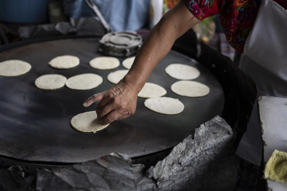 Felipa de Jesus Otzoy, 55, flips corn tortillas cooking on a hot comal at her market stall in Guatemala City, Saturday, Oct. 16, 2021. Otzoy has been making the hand-made tortillas in the same place for 35 years. (AP Photo/Moises Castillo)