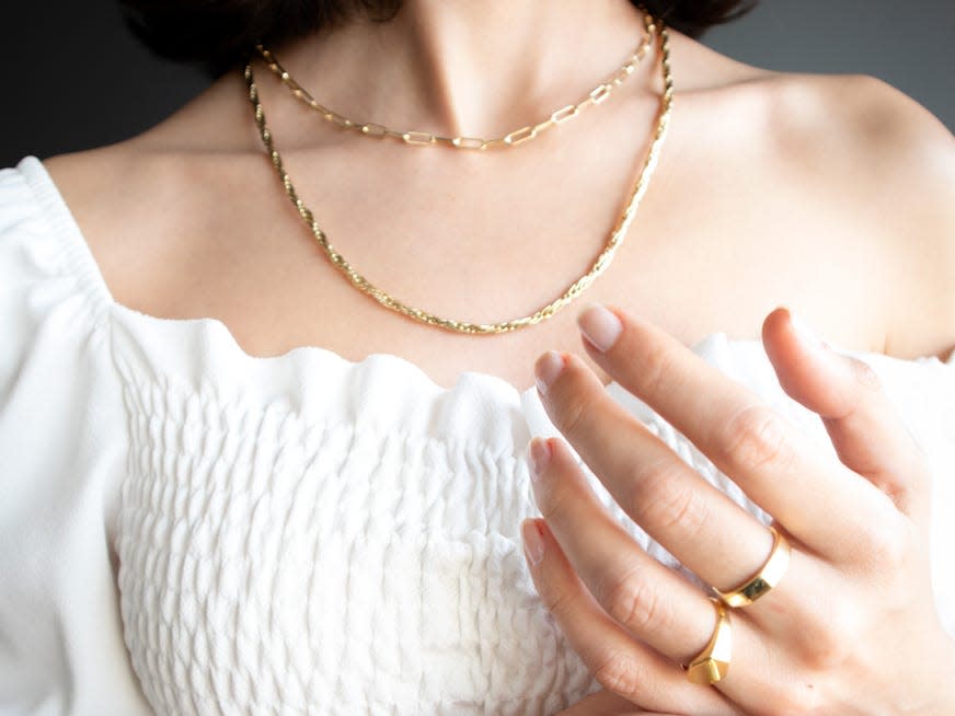 woman posing wearing a white blouse and gold necklaces and rings