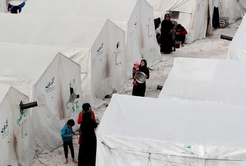 Internally displaced Syrians walk along tents in an IDP camp located in Idlib