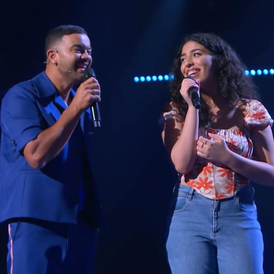 Guy Sebastian and Alisha George singing on the set of The Voice, Guy is wearing a blue outfit, Alisha is wearing an orange and white floral top with blue jeans. 