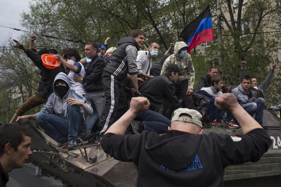 People greet pro-Russian activists atop of a government forces armored personal carrier captured from the enemy in fighting in Mariupol, eastern Ukraine, Friday, May 9, 2014. Fighting exploded Friday in Mariupol, a city of 500,000 on the Sea of Azov that is on the main road between Russia proper and Crimea. The fighting between government forces and insurgents in Mariupol has left several people dead. (AP Photo/Alexander Zemlianichenko)