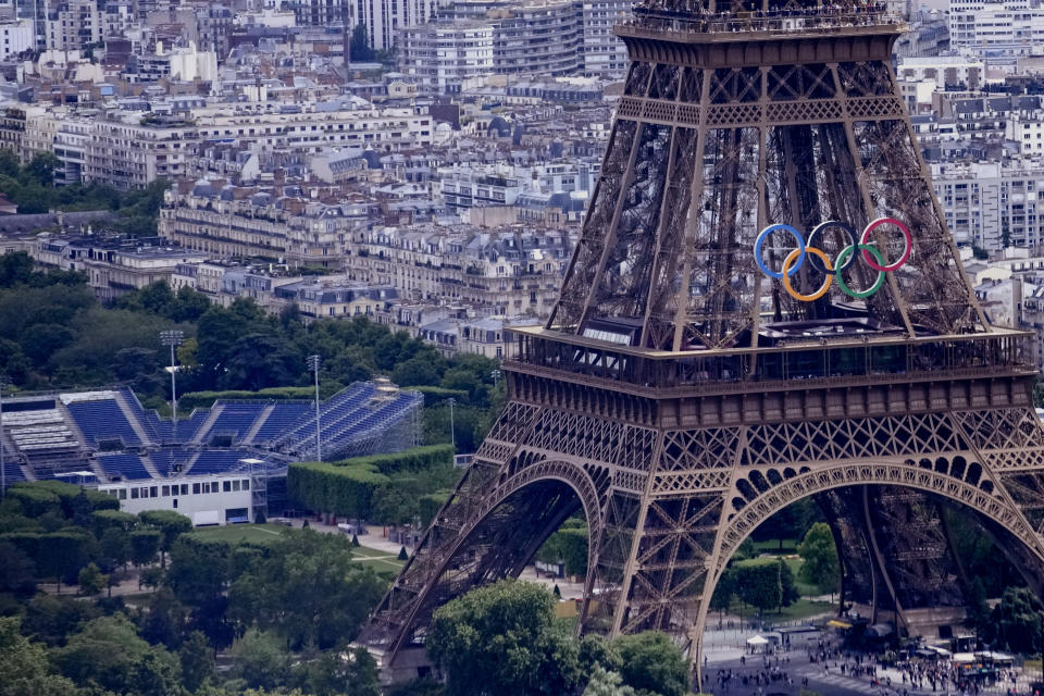 The Olympic rings are seen on the Eiffel Tower in Paris, France, Monday, June 17, 2024. The Champ-de-Mars at left will host the Beach Volleyball and Blind Football at the Paris 2024 Olympic and Paralympic Games. (AP Photo/Christophe Ena)