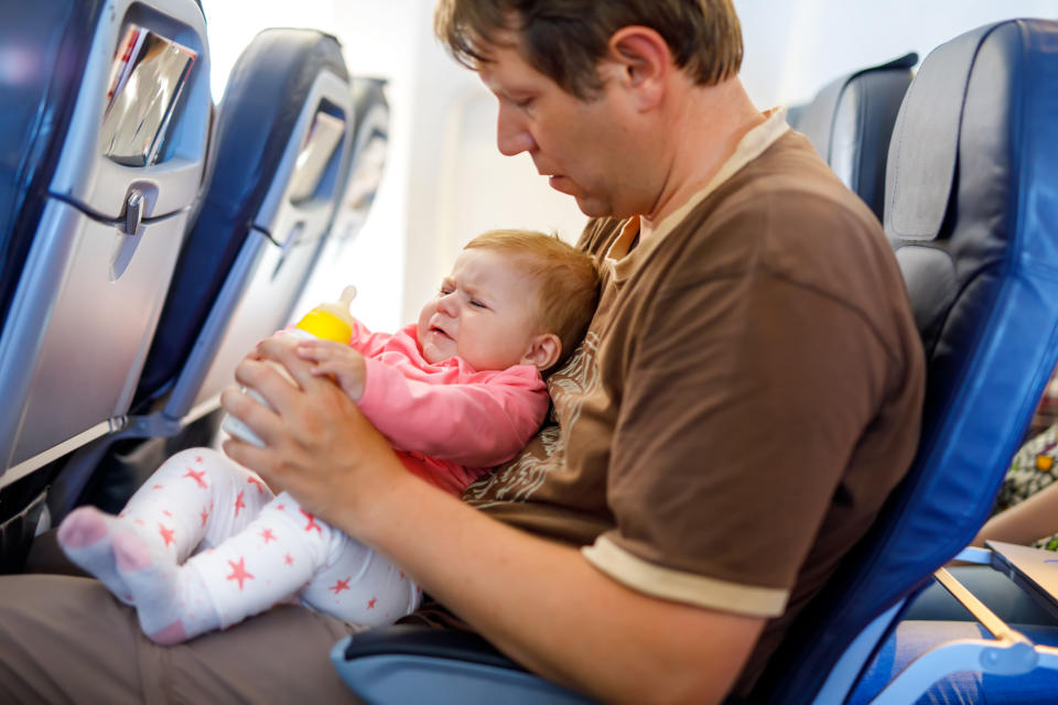 Father holding baby daughter during flight on airplane going on vacations. Baby girl drinking formula milk from bottle. 