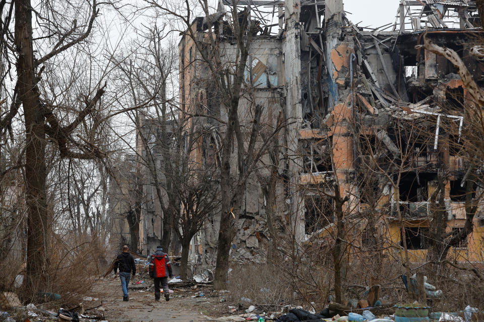 Men walk near multi-storey apartment blocks, which were destroyed in the course of Russia-Ukraine conflict, in Mariupol, Russian-controlled Ukraine, March 16, 2023. REUTERS/Alexander Ermochenko