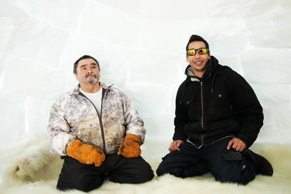 Ross Flowers, left, and Mark Nochasak sit on a polar bear hide inside the igloo outside of Flowers' home in Hopedale. (Heidi Atter/CBC - image credit)