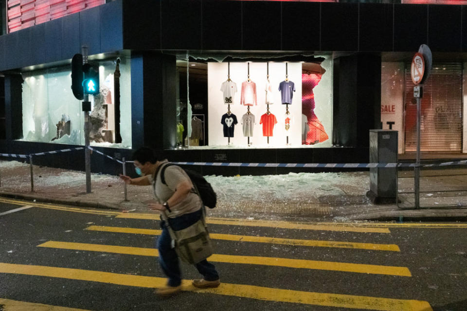 A man cautiously walks past a vandalised clothing shop during the anti-government rally. Source: Getty