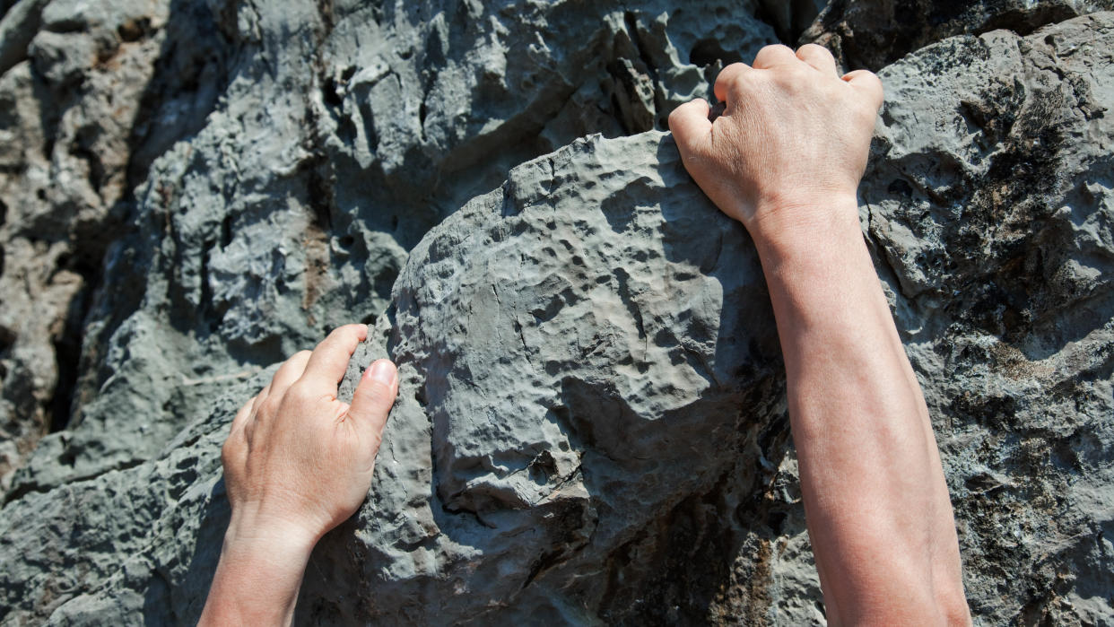  Man's hands climbing rock face. 