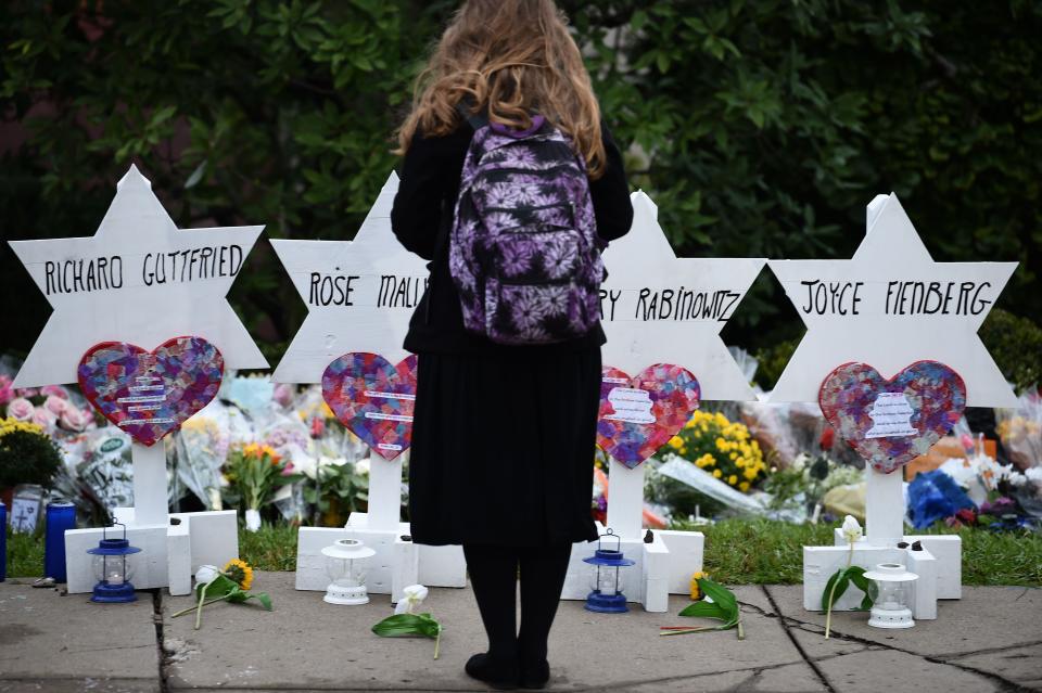 A person wearing a backpack in seen from behind observing a memorial for victims of the synagogue.