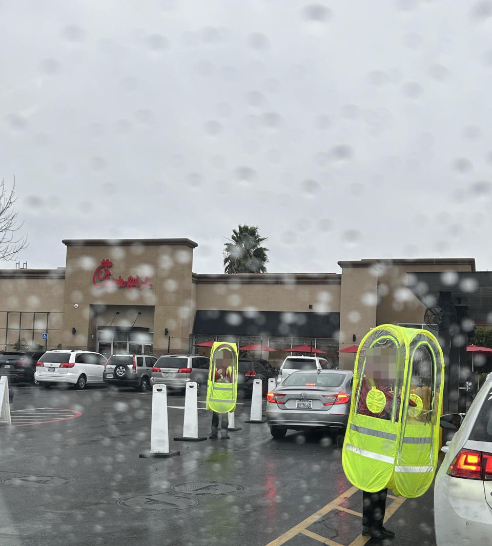 The Chick-fil-A parking lot in the rain, showing several people in neon-yellow, tubular bubbles with "windows"