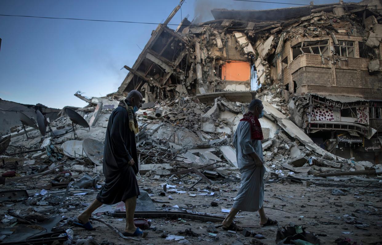 <p>Palestinians walk next to the remains of a destroyed building after Israeli air strikes on Gaza City</p> (AP/Khalil Hamra)