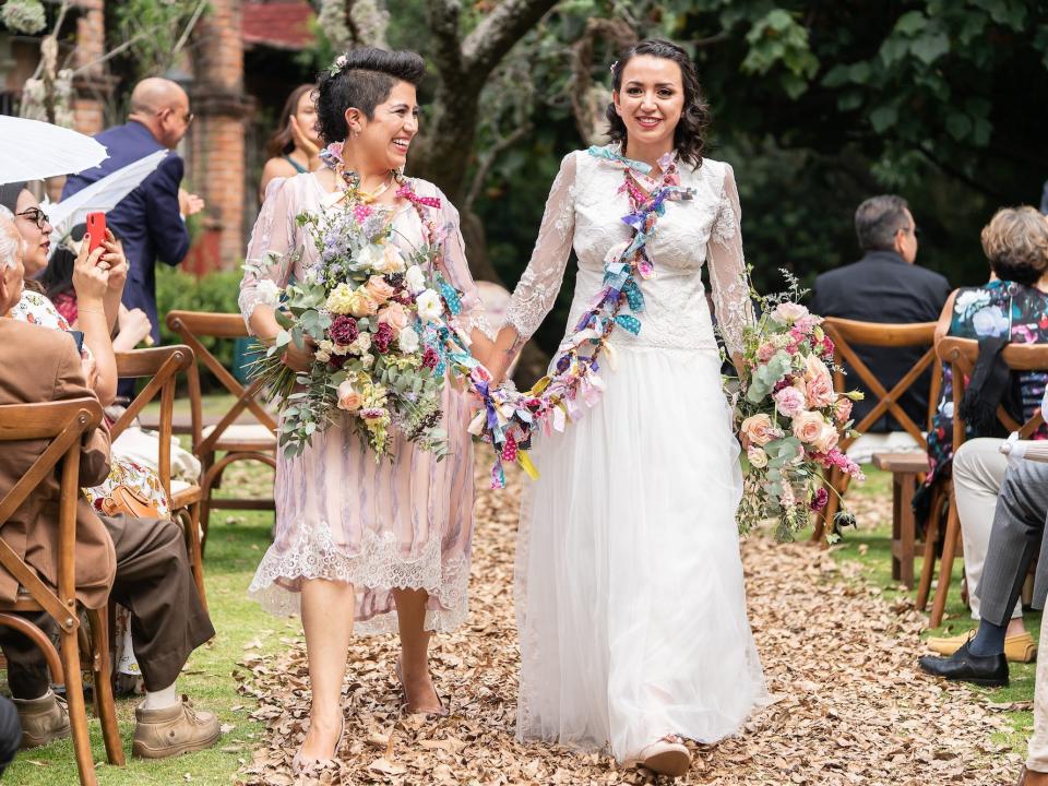 Two brides hold hands as they leave their wedding ceremony.