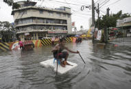 FILE - In this July 8, 2016, file photo, a man uses sticks to move a styrofoam block he is riding along a flooded road in suburban Mandaluyong, east of Manila, Philippines, as monsoon downpours intensify while Typhoon Nepartak exits the country. The virus outbreak is compromising the ability of nations to prepare for natural disasters and deal with the aftermath. Every year, the world contends with devastating typhoons, wildfires, tsunamis and earthquakes. (AP Photo/Aaron Favila, File)