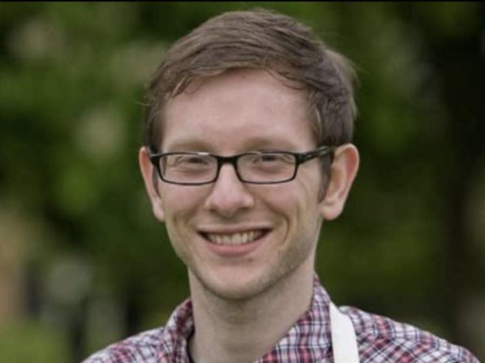 Edd Kimber smiling in glasses, a plaid shirt, and white apron.